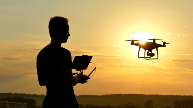 Der-Mann-spielt-mit-ein-Quadrocopter-auf-dem-Sonnenaufgang-Hintergrund