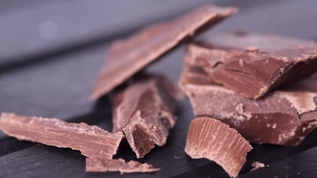 Panning-footage,-closeup-macro-of-chocolate-pieces-on-a-dark-wooden-table-background