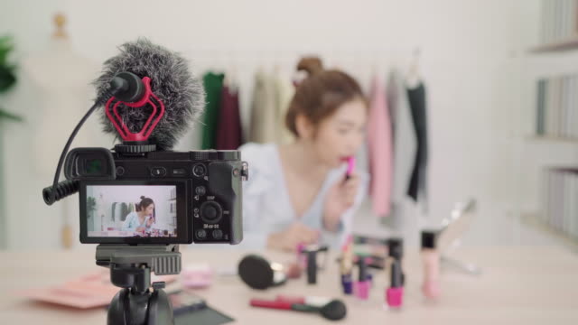 Beauty-blogger-present-beauty-cosmetics-sitting-in-front-camera-for-recording-video.-Beautiful-asian-woman-use-brush-while-review-make-up-tutorial-broadcast-live-video-to-social-network-by-internet.