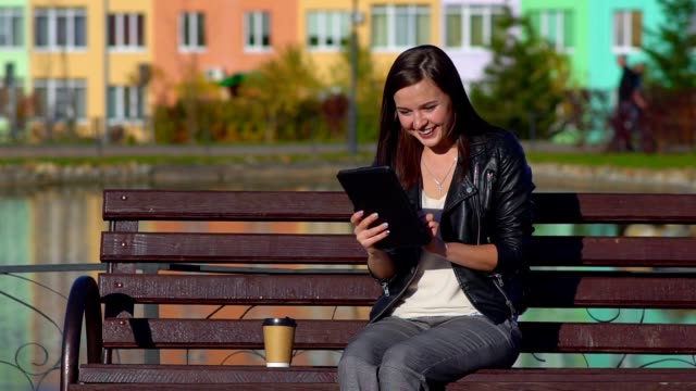 La-chica-en-el-parque-en-una-banca,-sosteniendo-una-tableta,-ver-las-redes-sociales.