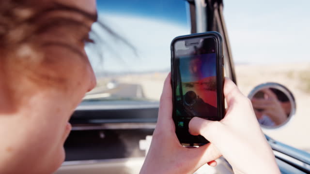 Woman-in-front-passenger-seat-of-open-car-filming-with-phone
