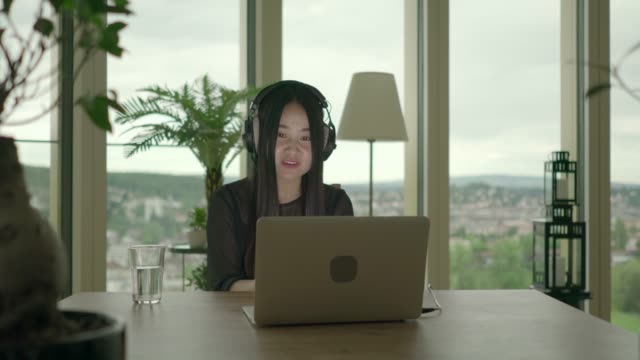 Junge-asiatische-Frau,-die-beim-Musikhören-über-Kopfhörer-am-Laptop-tippen