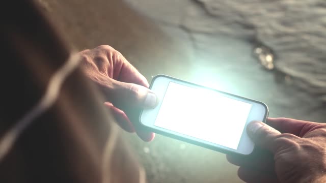 Glowing-futuristic-smartphone-being-held-by-man-on-beach---Tech-Concept