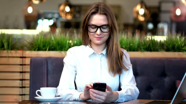 Portrait-of-stylish-woman-wearing-glasses-and-white-shirt-typing-message-using-smartphone