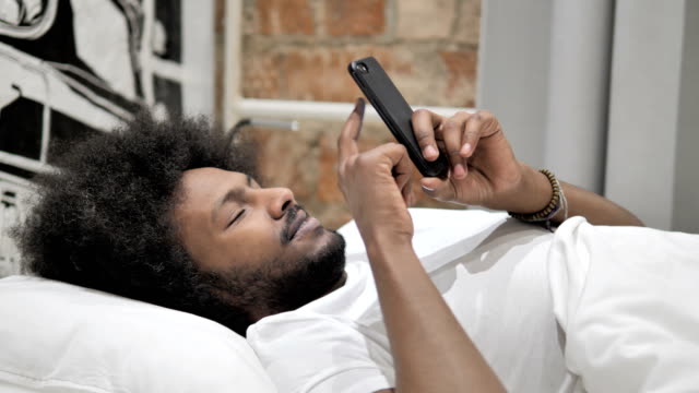 Afrikanischer-Mann-mit-Smartphone,-Liegen-im-Bett