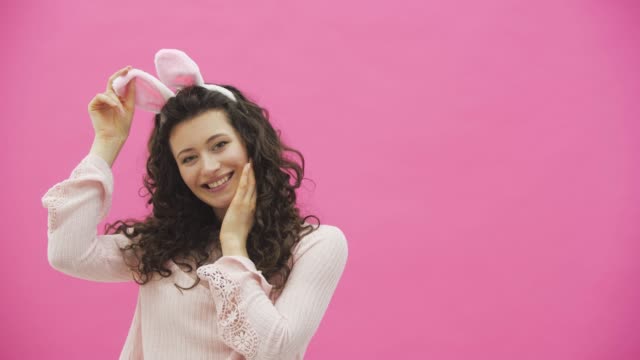 Festive-Easter-holiday-season.-Smiling-young-woman-in-Easter-bunny-ears-on-pink-background-jumping-and-looking-at-copy-space.