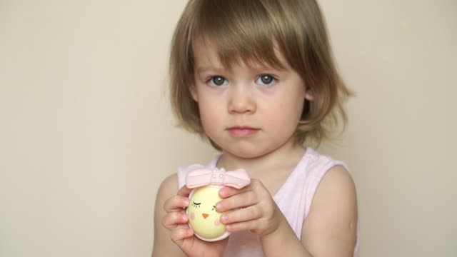 Portrait-of-little-pretty-smiling-caucasian-girl-holds-in-hand-chicken-egg-decorated-for-Easter-chick,-with-painted-muzzle-with-eyes.