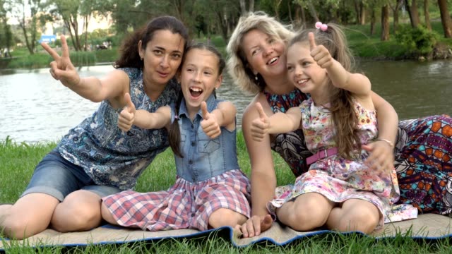 Close-up,-mothers-with-young-daughters-play-and-have-fun-sitting-on-the-lawn-in-the-Park-at-sunset-on-a-summer-day-by-the-river.-Family-outdoor-recreation.-The-concept-of-family-happiness.-4K.