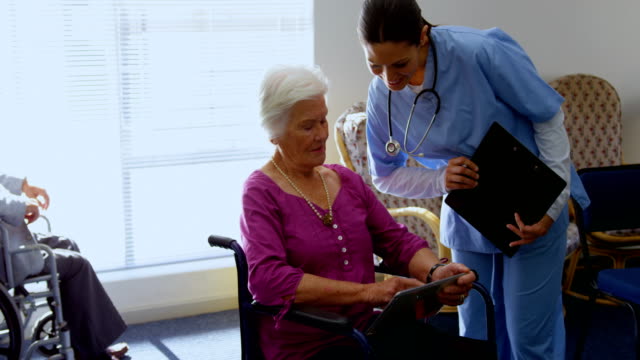 Frontansicht-von-kaukasischer-Ärztin-und-Seniorenfrau,-die-über-digitales-Tablet-in-der-Krankenpflege-diskutiert