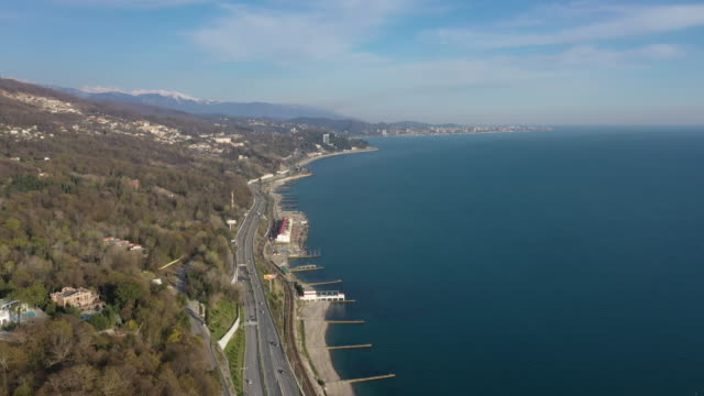 Aerial-video-shooting.-The-black-sea-coast-of-Sochi-from-a-height.-The-camera-is-moving-from-the-shore.-Coastline.-The-road-along-the-seashore.-Mountains-Of-Krasnaya-Polyana.