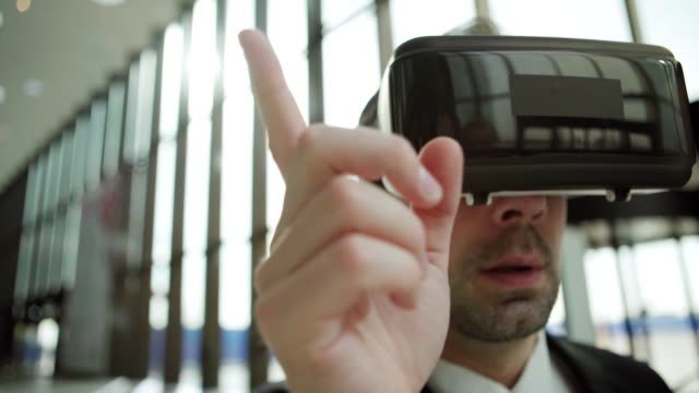 Close-up-of-middle-aged-businessman-in-virtual-reality-headset-working-with-visualized-analytical-data-in-office-hall