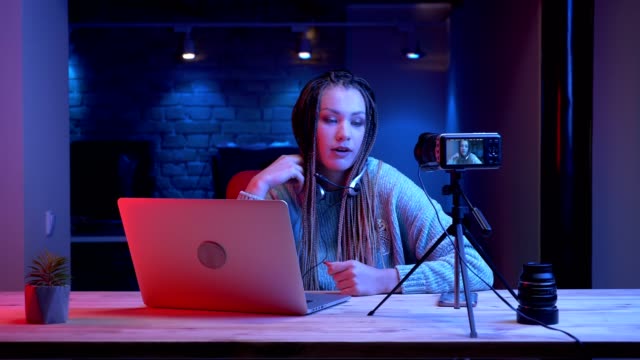 Closeup-shoot-of-young-attractive-female-blogger-with-dreadlocks-in-headphones-playing-video-games-with-the-neon-background-indoors