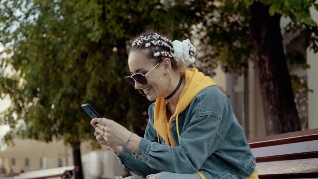Joven-mujer-sonriente-usando-teléfono-inteligente-sentado-en-el-banco.-Mensajes-de-texto-femeninos-con-teléfono