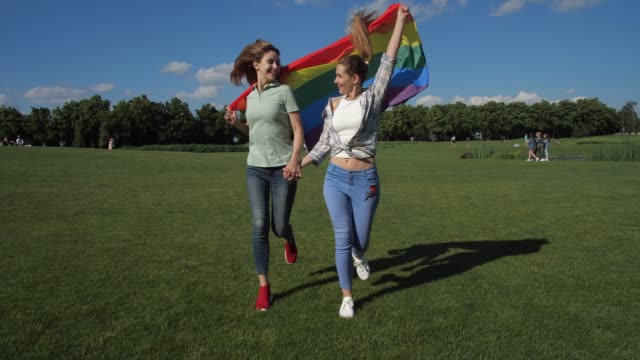 Glückliche-Lesben-mit-Regenbogen-Flagge-läuft-im-Park