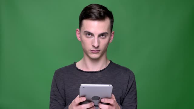 Nahaufnahme-von-jungen-stattlichen-kaukasischen-Männlichen-mit-dem-Tablet-blickend-auf-die-Kamera-und-lächelnd-mit-Hintergrund-isoliert-auf-grün