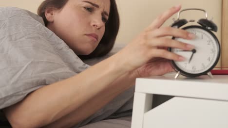 Woman-wakes-up-from-alarm-clock-and-checks-her-mobile-phone-in-bed