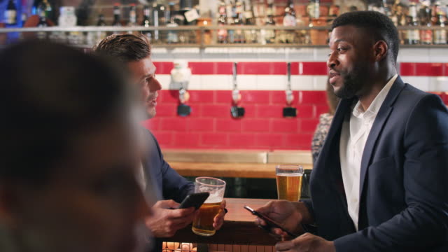 Dos-empresarios-revisan-los-teléfonos-móviles-mientras-se-reúnen-para-beber-en-el-bar