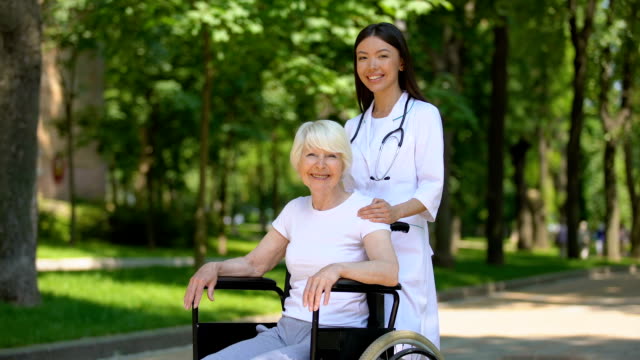 Enfermera-y-mujer-discapacitada-sonriendo-a-la-cámara,-relajarse-en-el-parque-del-hospital
