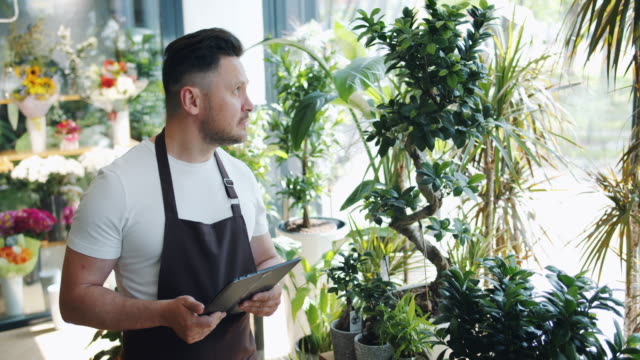 Happy-male-florist-working-with-tablet-in-flower-shop-smiling-looking-at-plants