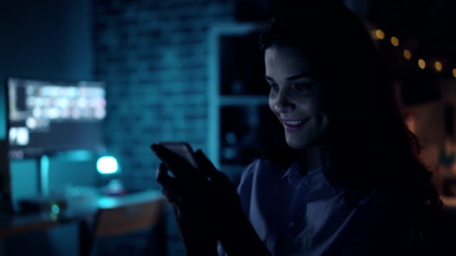Glückliches-Mädchen-mit-Smartphone-beobachten-Inhalte-auf-dem-Bildschirm-in-dunklen-Büro-in-der-Nacht