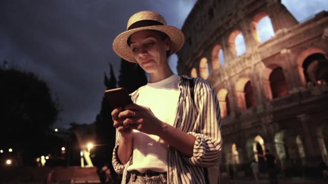 Fröhliche-kaukasische-Millennial-Weibliche-Reisende-lesen-Nachricht-auf-Smartphone-mit-4G-verbunden-im-Roaming-während-der-Freude-Anreise-nach-Rom-am-Abend
