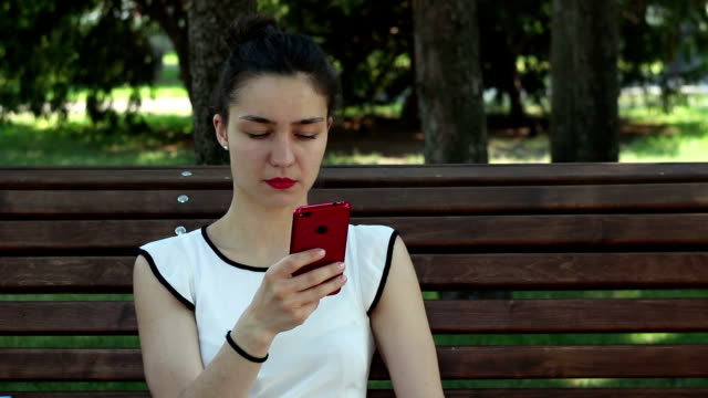 Joven-hermosa-chica-hablando-por-teléfono-mientras-está-sentada-en-un-banco-del-parque.