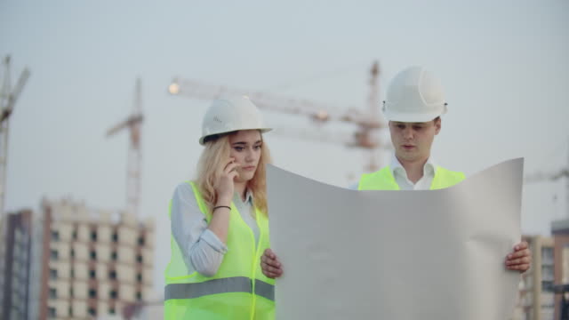 Mujer-hablando-por-teléfono-y-pregunta-al-Constructor-lo-que-está-en-los-dibujos-de-pie-en-el-fondo-de-los-edificios-en-construcción