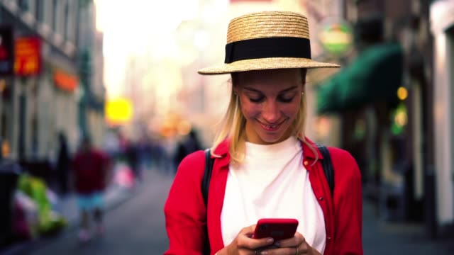Kaukasien-junge-Frau-in-trendigen-Hut-und-Casual-Wear-Überprüfung-Benachrichtigung-auf-Handy,-während-auf-der-Straße-stehen