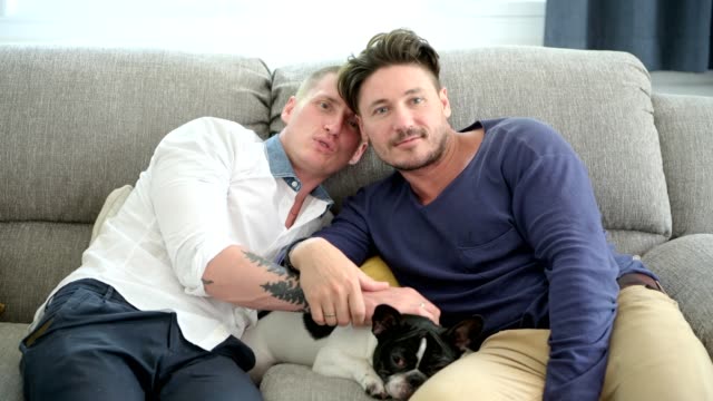 Gay-couple-relaxing-on-couch-with-dog.-Comforting-their-dog.