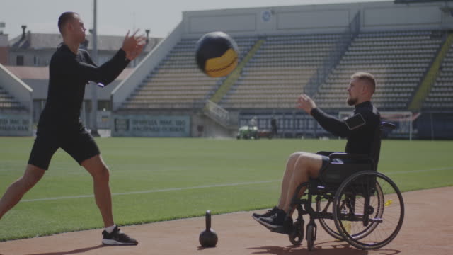 Atleta-en-silla-de-ruedas-y-entrenador-lanzando-pelota-de-medicina
