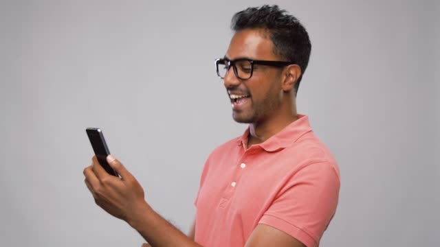 glücklicher-indischer-Mann-in-Derbrille-mit-Smartphone