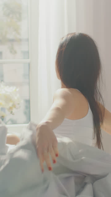 Beautiful-Brunette-Slowly-Waking-up-in-the-Morning,-Stretches-and-Gets-Up-from-the-Bed,-Sun-Shines-on-Her-From-the-Big-Window.-Video-Footage-with-Vertical-Screen-Orientation-9:16