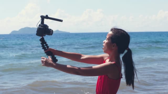Portrait-of-a-young-female-vlogger-holding-DSLR-Camera-with-tripod-and-filming.