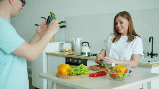 Hausfrau-macht-Salat-Spaß,-während-Mann-Fotografieren-mit-Smartphone
