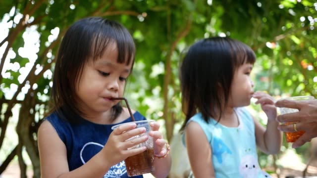 Pequeña-niña-asiática-bebiendo-su-bebida-mientras-está-sentada-en-el-parque-el-día-de-verano.-Enfoque-selectivo.