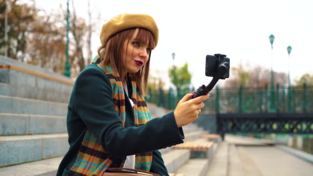 Junge-Vlogger-Streaming-aus-öffentlichen-Park-mit-Smartphone-und-Steadicam