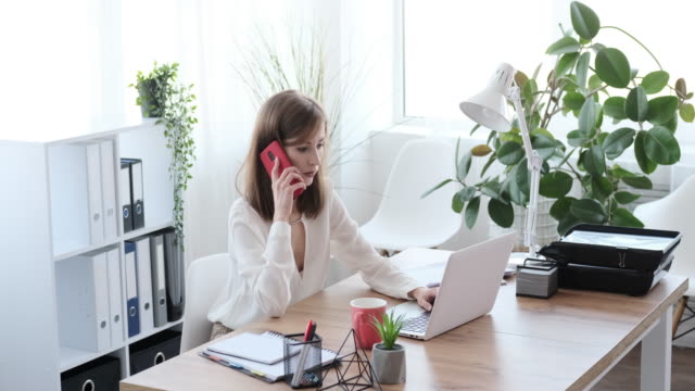 Businesswoman-talking-on-mobile-phone-while-working-on-office-laptop