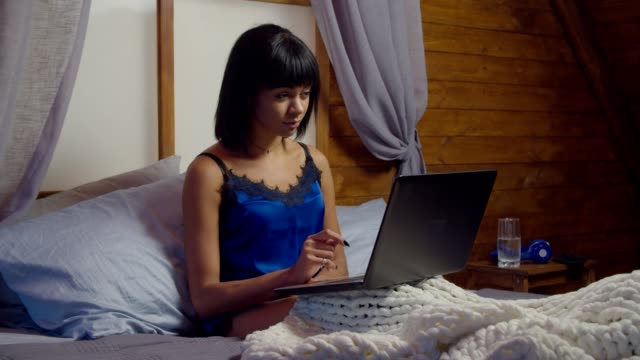 Encantadora-mujer-en-pijama-trabajando-en-la-computadora-portátil-en-la-cama