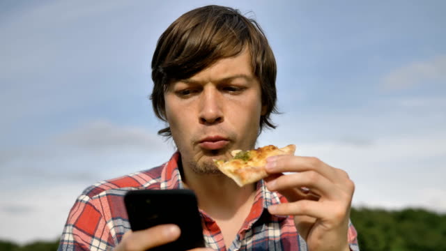 Mann-surft-Internet-mit-Telefon-essen-Pizza-in-grünen-Park