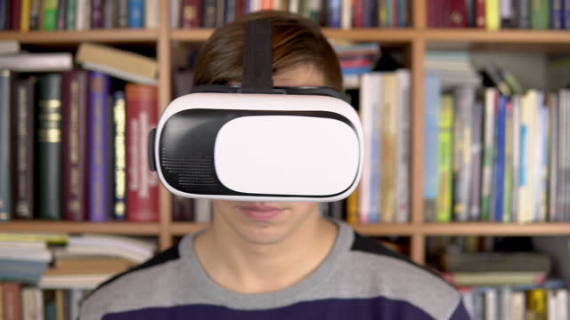 Ein-junger-Mann-liest-in-der-Bibliothek-ein-Buch-mit-VR-Brille.-Ein-Mann-mit-VR-Helm-auf-dem-Kopf-blättert-in-der-virtuellen-Realität-durch-Seiten.-Im-Hintergrund-sind-Bücher-über-Bücherregale.-Buchbibliothek.