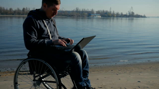 Disabled-man-in-wheelchair-works-on-laptop-by-the-river