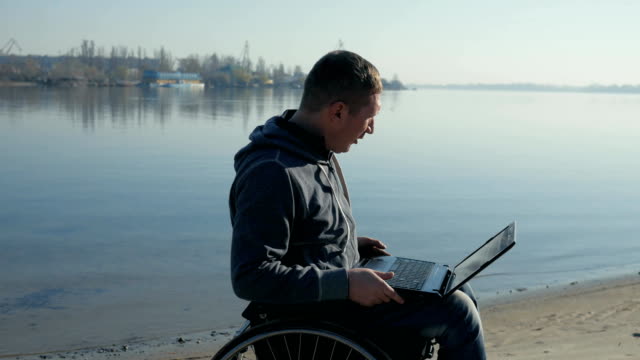 Disabled-person-in-wheelchair-with-laptop-leads-video-chat,-alone-by-the-water