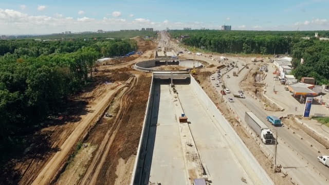 drone-is-flying-along-construction-of-roads-and-brand-new-traffic-circle,-cars-are-moving-in-detour