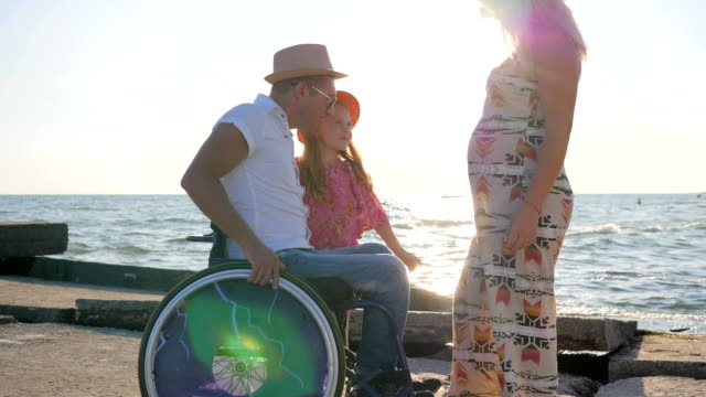 dad-And-Child-hold-to-mothers-belly,-man-in-wheelchair-with-little-Girl-and-pregnant-woman