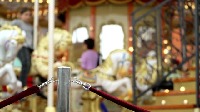 Merry-go-round-carousel.-Happy-kids-with-parents-riding-carousel-and-taking-pictures-and-selfies,-rope-fence-made-from-red-velvet,-employee-closes-door