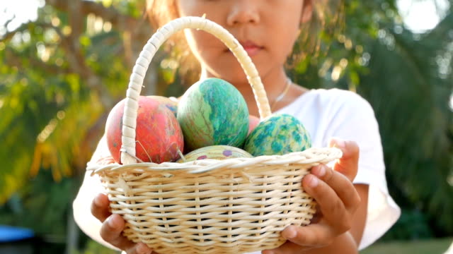 Close-up-of-children-hand-holding-a-basket-with-easter-eggs-in-sunshine-background