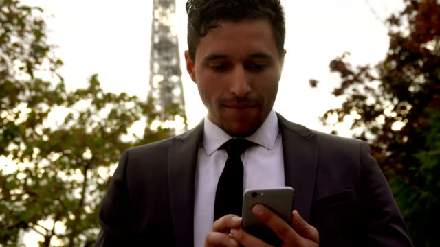 Mann-in-einem-Anzug-mit-Anwendung-auf-einem-Smartphone-neben-dem-Eiffel-Turm