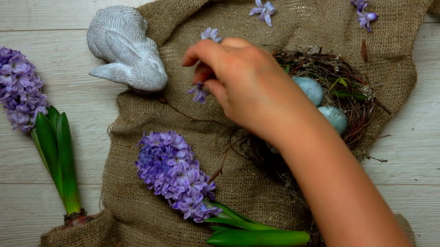 Tisch-mit-Osternest-mit-bunten-Eiern-und-Blumen-dekorieren-Hände