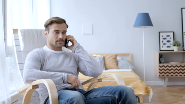 Hombre-adulto-hablando-por-teléfono-mientras-relajante-en-silla