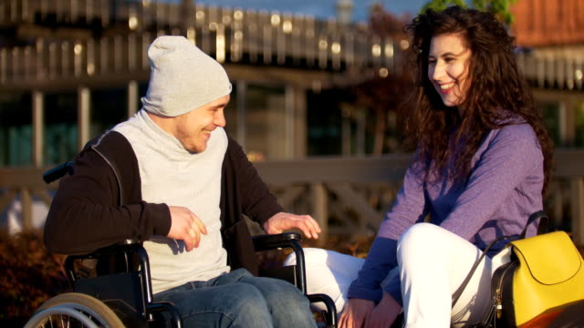 Happy-couple---disabled-young-man-in-a-wheelchair-with-young-woman-enjoying-the-sunset-together